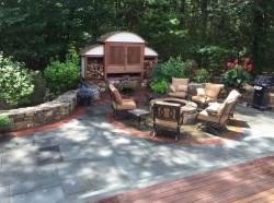 A backyard outdoor room featuring a bluestone patio, stone walls, fire pit, and TV enclosure
